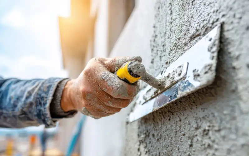 Ein Stukkateur verputzt eine Wand mit rauhem Putz - Bildausschnitt Hand mit Kelle