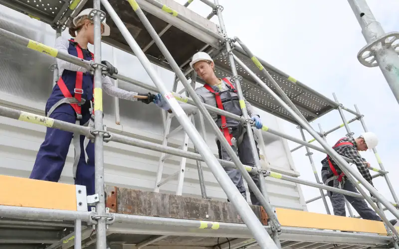 Drei Stukkateure stehen auf einem Gerüst und bauen es auf